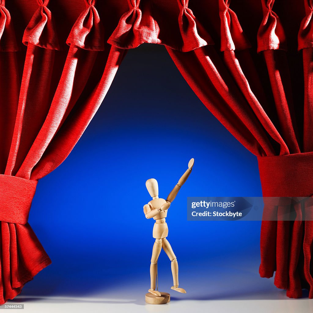 A wooden actor figurine on a stage surrounded by red curtains