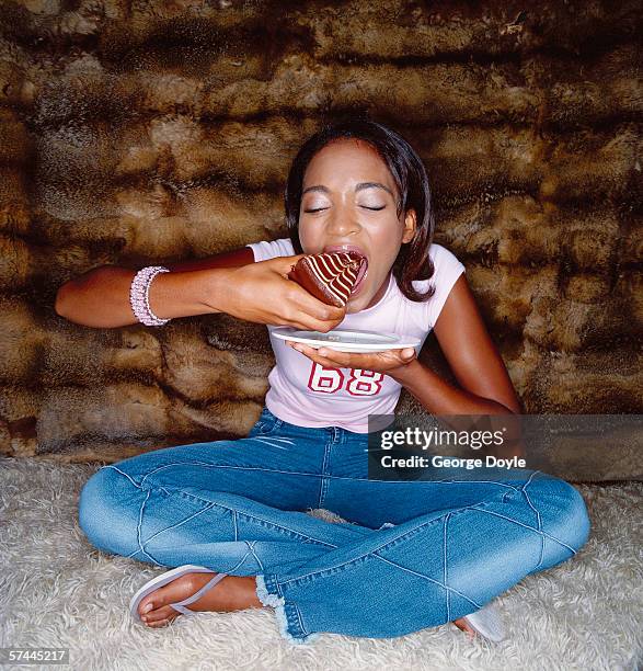 a young woman sitting on the floor and eating a piece of cake - jeans cake foto e immagini stock