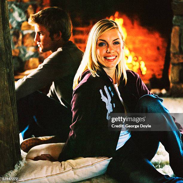 a young couple sitting back to back in front of a fire place - woman back pillow blonde stock pictures, royalty-free photos & images