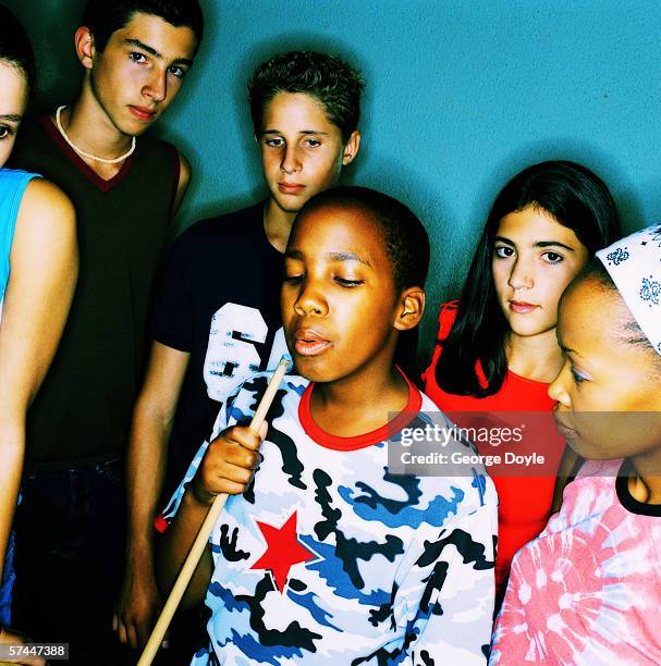 view of a teenaged boy blowing on a pool stick with his friends standing around him - pool stockfoto's en -beelden