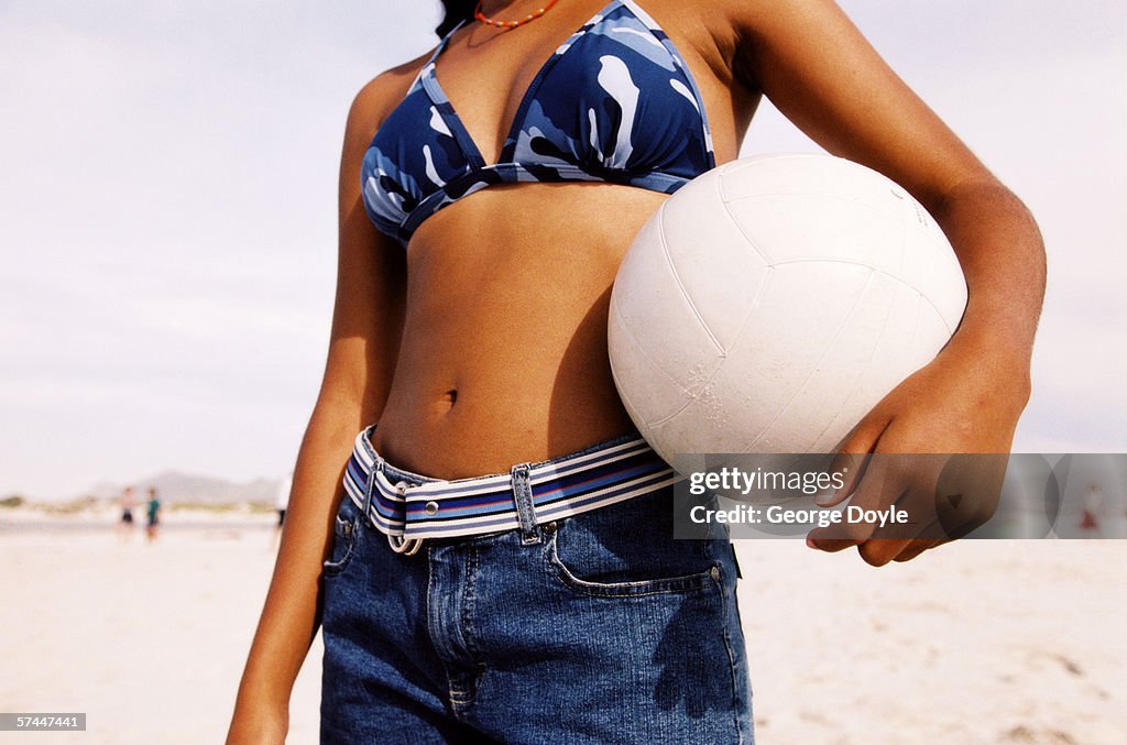 Close-up of a young woman's bare midriff with her arm holding a ball to it
