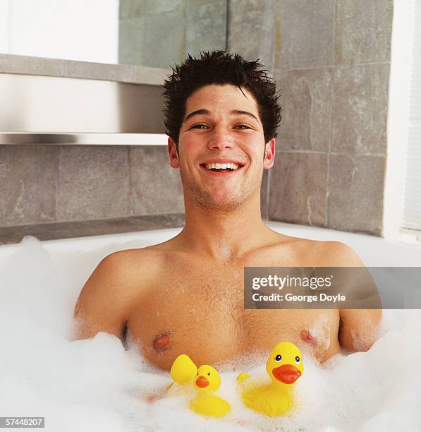 portrait of a man sitting in a bubble bath with rubber ducks - bath bubble stockfoto's en -beelden
