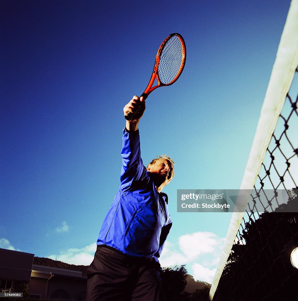 Low angle view of a man holding up a tennis racket next to the court net