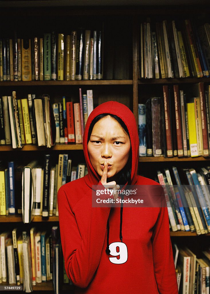 Portrait of a young woman wearing a hooded jacket and making the sign for no noise