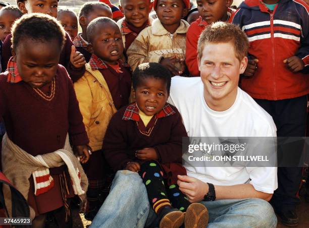 Britain's Prince Harry wears a shirt with the Sentebale logo as he holds a small girl while on visit to the Good Shepherd home, during a return visit...