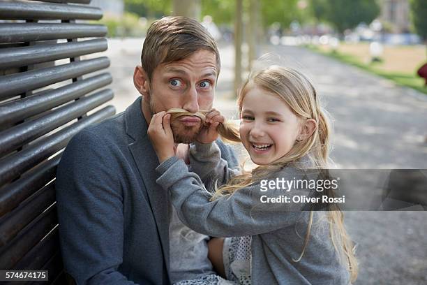 playful girl with father on bench - konzepte und themen stock-fotos und bilder