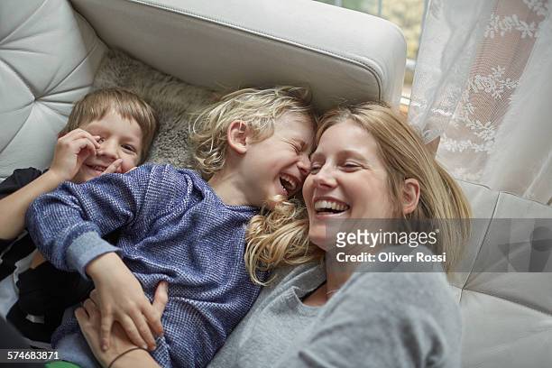 laughing mother with two sons on couch - blue sweater stockfoto's en -beelden