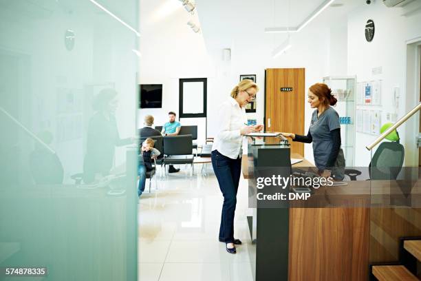 mature female patient at dental clinic - woman filling out paperwork stockfoto's en -beelden