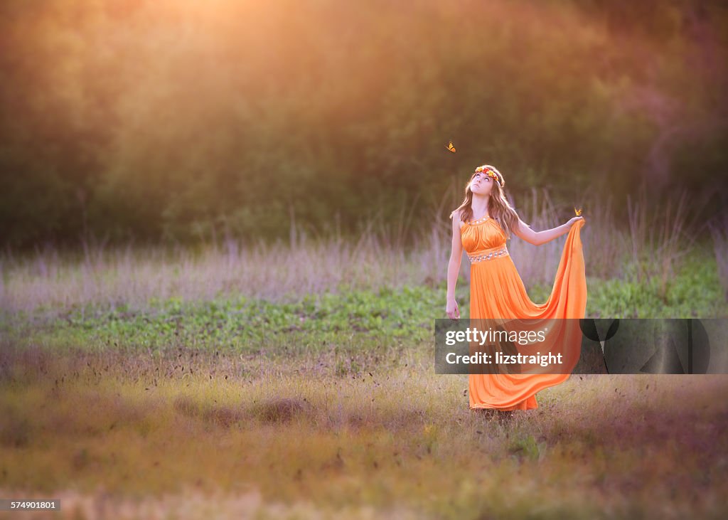 Girl standing in a field holding the hem of her dress