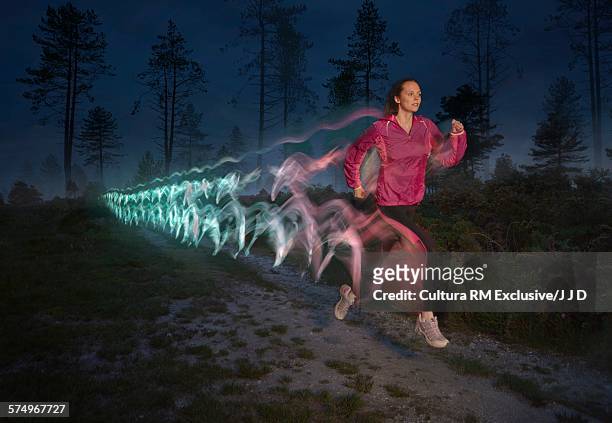 young woman followed by light trails running on forest dirt track at night - effortless imagens e fotografias de stock