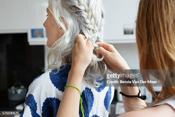close up of woman plaiting senior woman's hair - braid stock-fotos und bilder