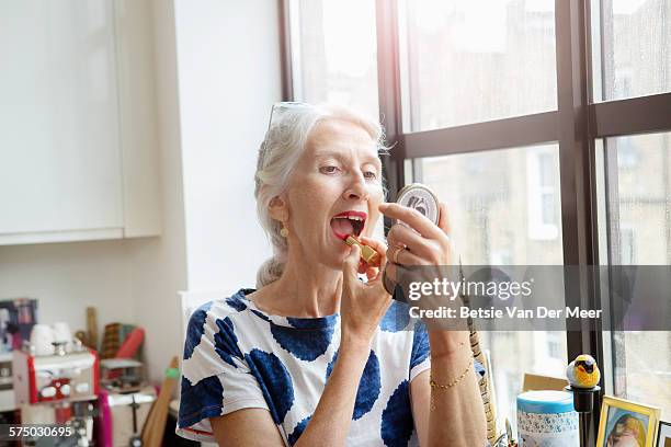 Mature woman putting on lipstick at home