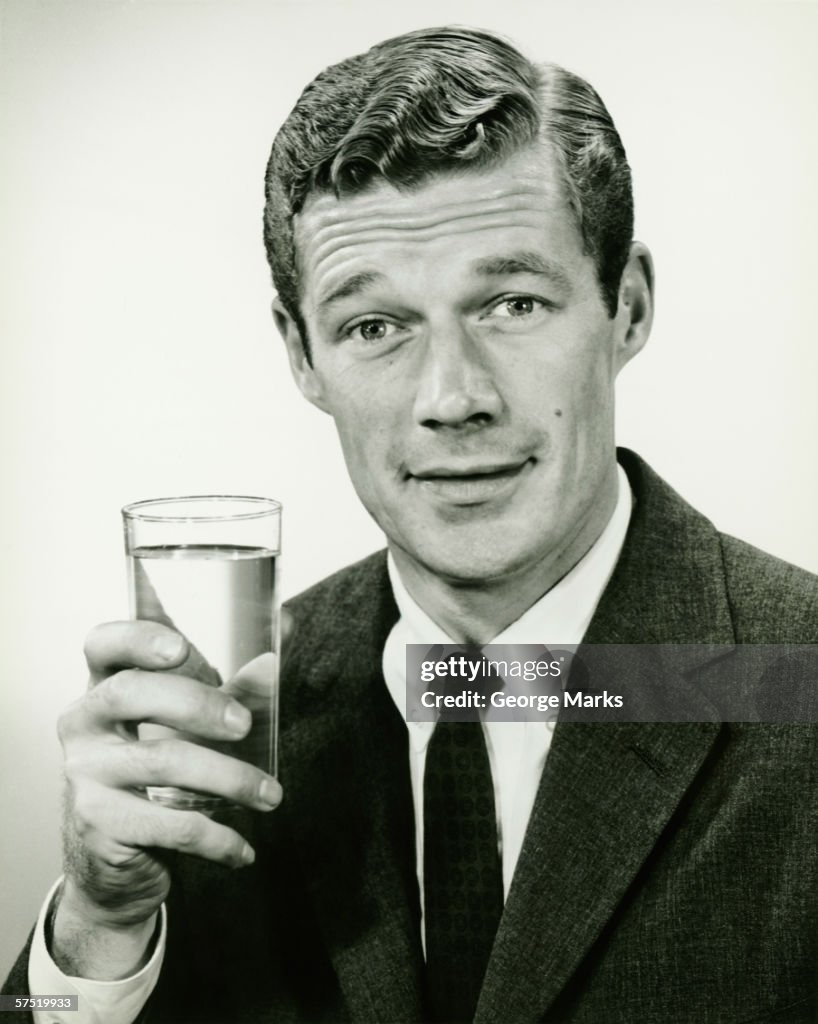 Young businessman holding glass of water, posing in studio, (B&W), portrait
