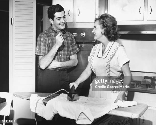 young couple in kitchen, woman ironing, (b&w) - housewife stock pictures, royalty-free photos & images