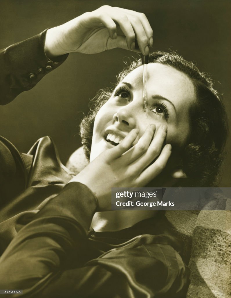 Woman using eye drop in studio, (B&W)