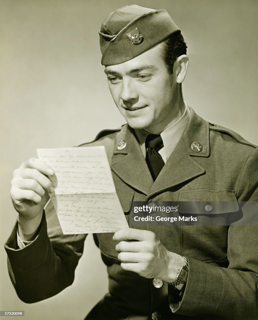 World War II Army solider reading letter in studio, (B&W), portrait