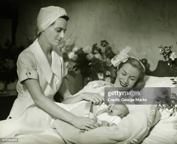 mother lying in bed smiling to baby-child (0-6 months), nurse standing beside, (b&w) - 1930 stockfoto's en -beelden