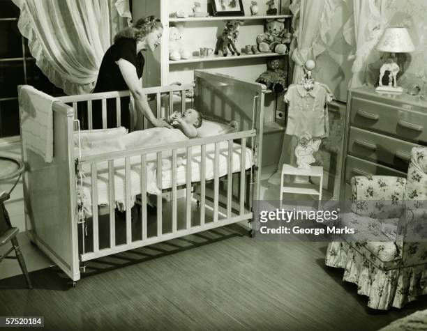 mother looking at baby (3-6 months) lying in crib, (b&w) - 1940s bedroom stock pictures, royalty-free photos & images