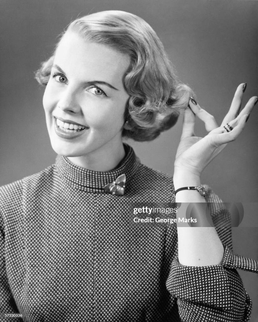 Smiling woman touching hair posing in studio, (B&W), portrait, close-up