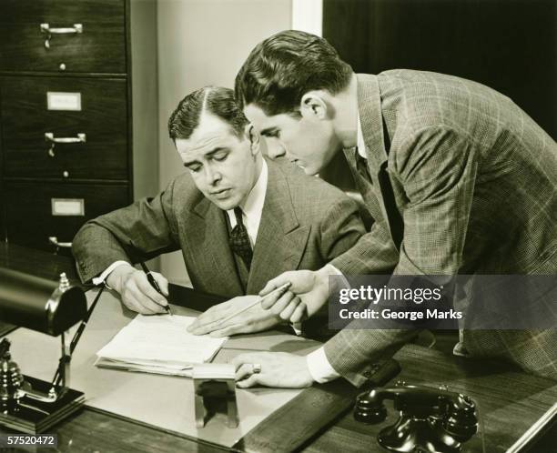 two young businessmen talking at small desk, (b&w) - vintage office stock pictures, royalty-free photos & images