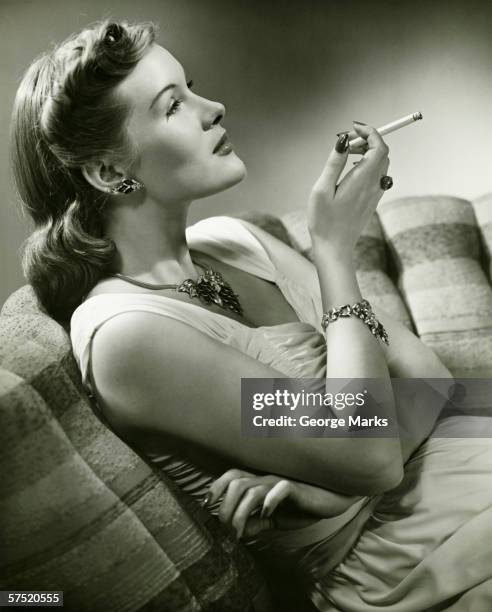 elegant woman sitting on couch, smoking cigarette, (b&w) - 1930s woman stock pictures, royalty-free photos & images