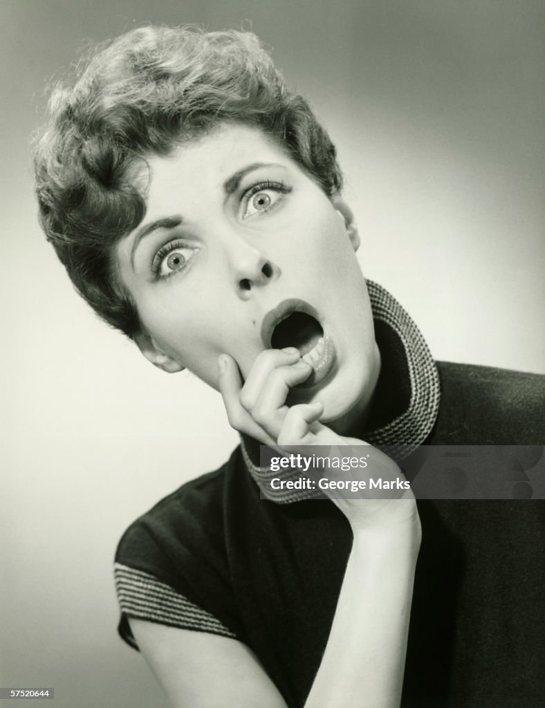 Shocked woman with fingers on lips in studio, (B&W), portrait
