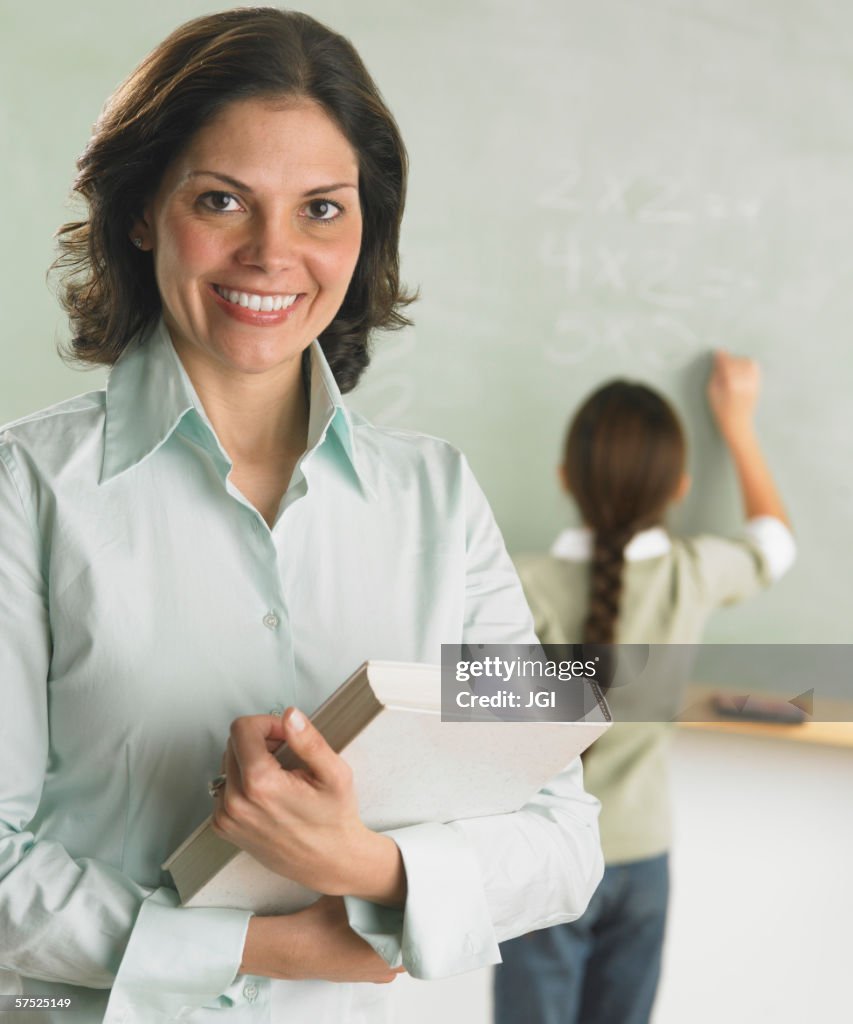 Teacher smiling for the camera as student works in the background