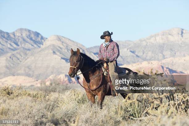 young man in a cowboy outfit riding a horse - black horse stockfoto's en -beelden