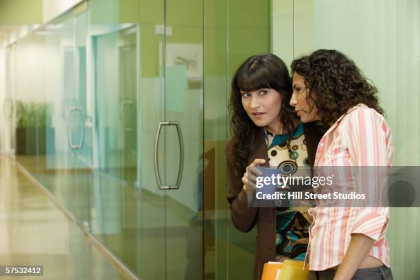 businesswomen gossiping in office hallway - cotilleo fotografías e imágenes de stock