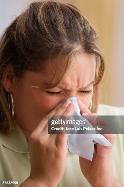young woman blowing her nose - closeup of a hispanic woman sneezing foto e immagini stock