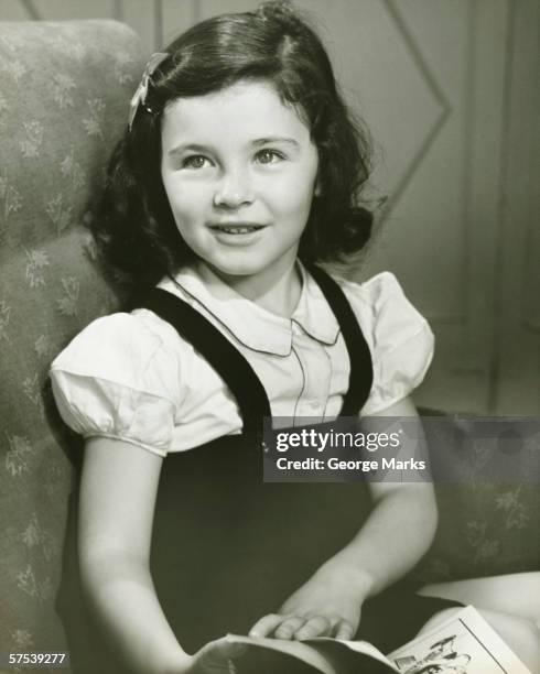 girl (6-7) sitting in armchair, holding opened book, (b&w) - 1940's stock pictures, royalty-free photos & images