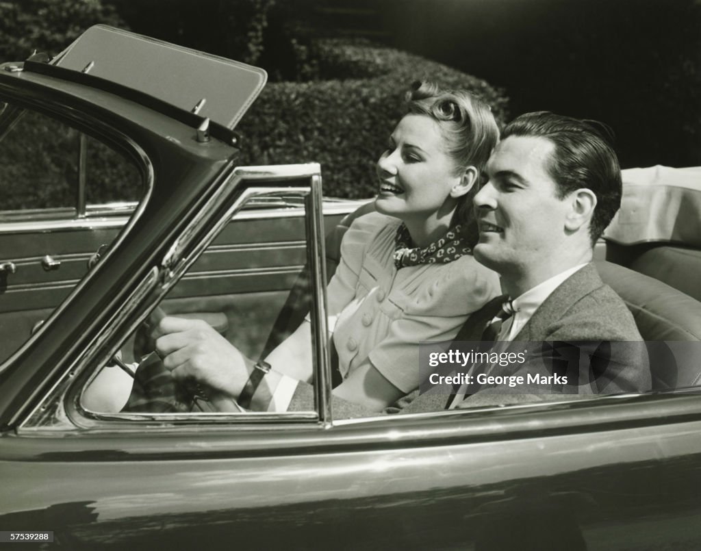Elegant couple riding in in convertible car, (B&W)