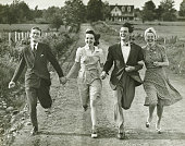 Two couples holding hands, running on footpath, (B&W)