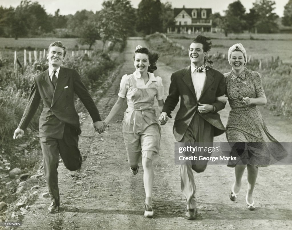 Two couples holding hands, running on footpath, (B&W)