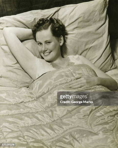 young woman lying in bed, smiling, (b&w), portrait - 1940s bedroom stock pictures, royalty-free photos & images