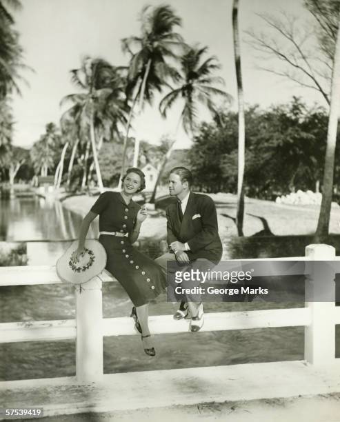 elegante par sentado en la valla en ambiente tropical, (b & p - george marks man fotografías e imágenes de stock