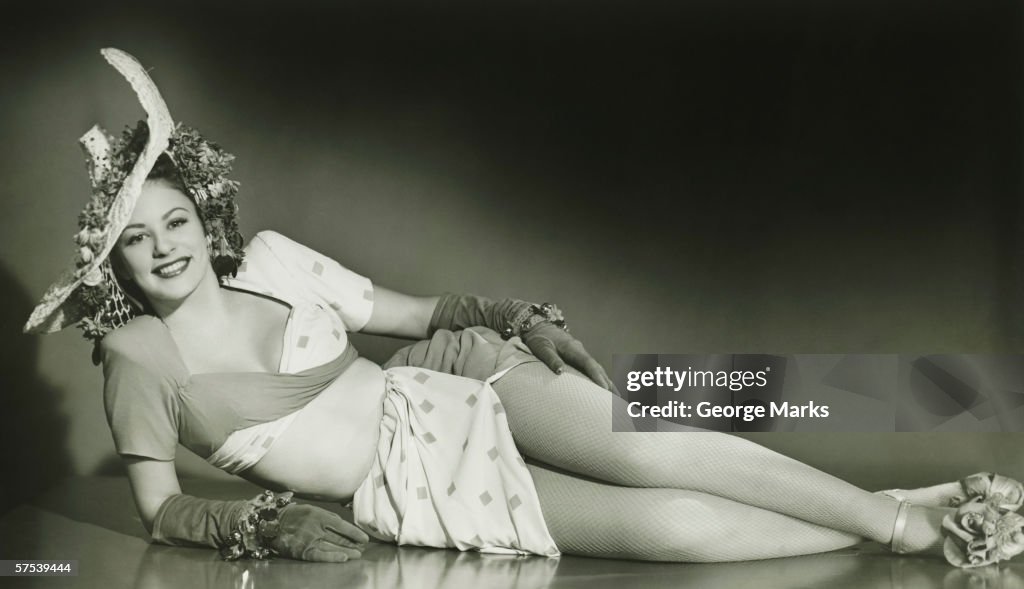 Young woman in fashionable hat lying down in studio, (B&W)