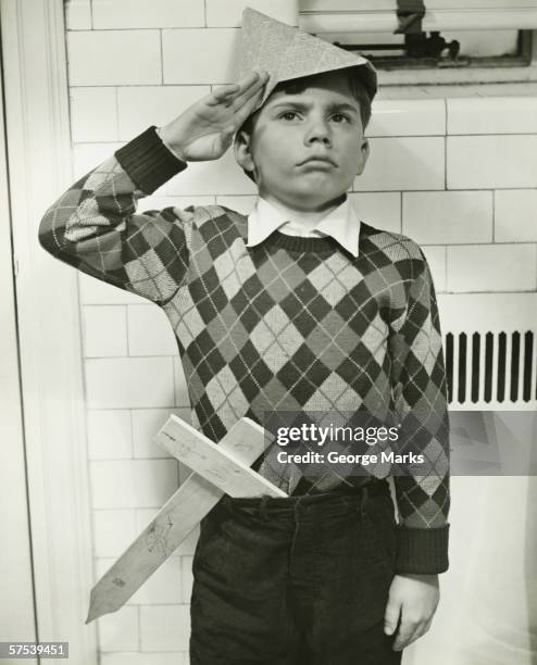 boy (8-9) with wooden sword saluting indoors, (b&w) - dressing up stock pictures, royalty-free photos & images