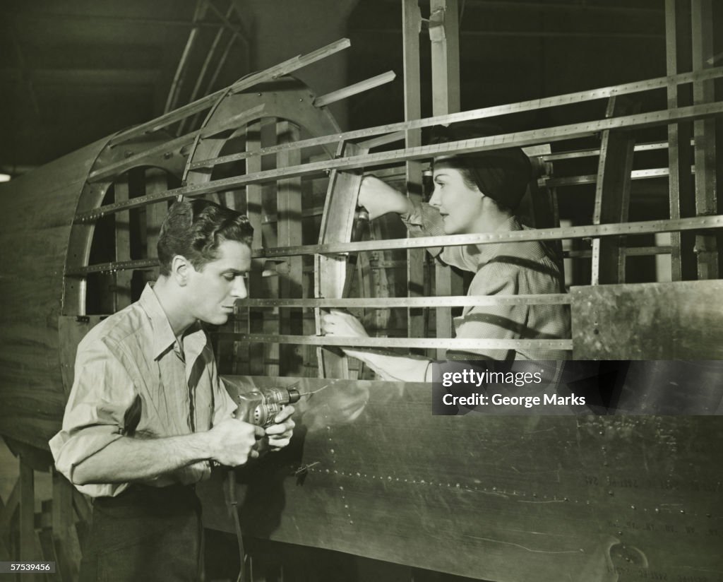 Young man and woman working in plane body in factory, (B&W)