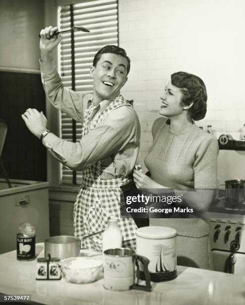 young cheerful couple in kitchen, man in apron, (b&w) - 1930s woman stock pictures, royalty-free photos & images