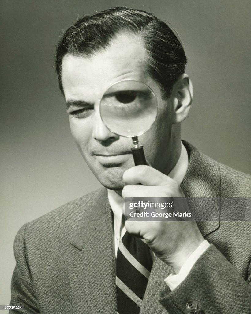 Businessman in full suit in studio looking through magnifying glass, (B&W), portrait