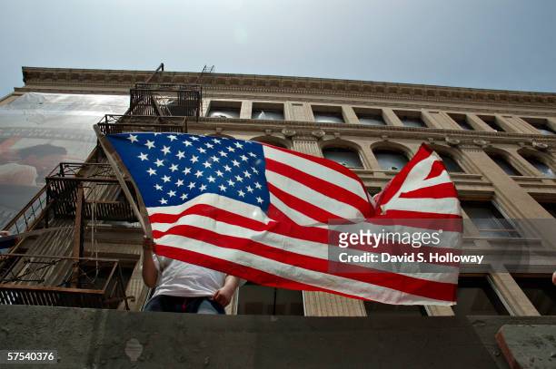 Man waves a mexican flag from a building as hundreds of thousands of immigrants demonstrate on May 1, 2006 in downtown Los Angeles, California. The...