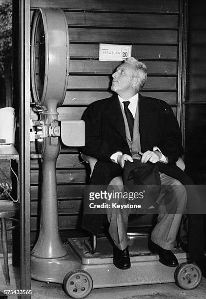 Actor Spencer Tracy checking his weight on a large set of scales, during a visit to the famous health resort of Montecatini near Florence, October...