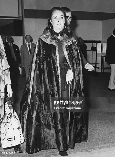 Actress Elizabeth Taylor wearing a long cape over knee-high boots and hot pants as she arrives at Heathrow Airport, London, October 13th 1971.