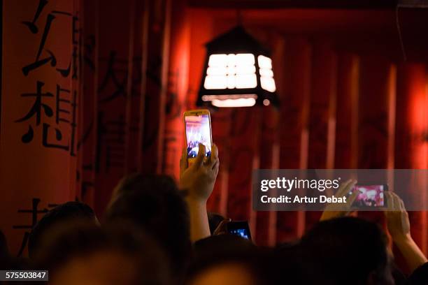 People with his smartphones with bright screen in the night taking pictures for sharing on the social media networking websites.