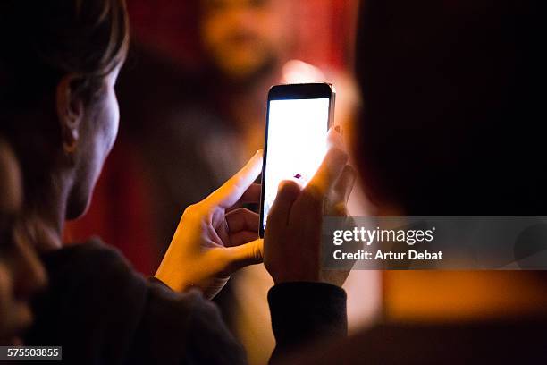 People with his smartphones with bright screen in the night taking pictures for sharing on the social media networking websites.