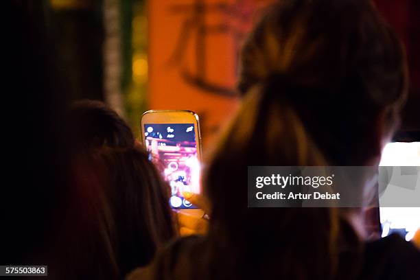 People with his smartphones with bright screen in the night taking pictures for sharing on the social media networking websites.