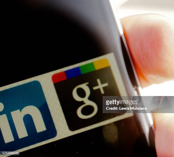 Social media. Extreme close up of fingers holding mobile phone with social media network classic icons visible on screen. LinkedIn and Google +