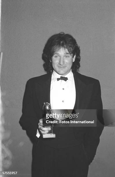 American comedian and actor Robin Williams, dressed in a three-piece tuxedo, holds a trophy backstage at the Golden Globes, Beverly Hilton, Beverly...
