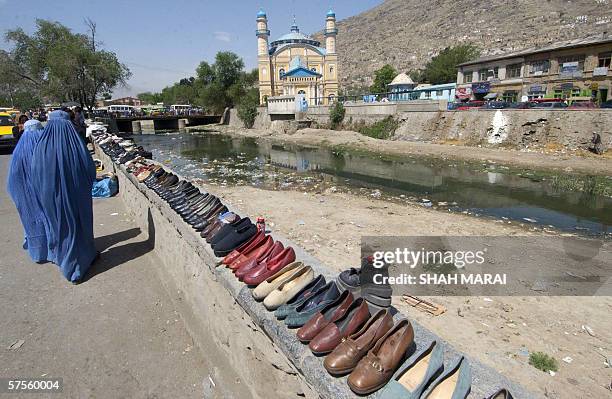 Two Afghan women wearing the traditional blue burqua walk past shoes for sale at a street market in the center of Kabul, 09 May 2006. The shoes were...
